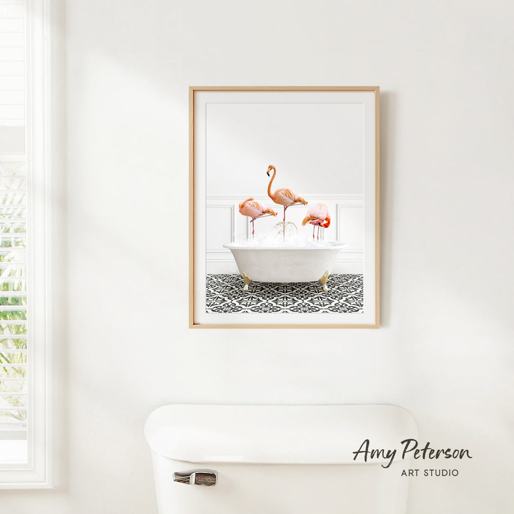 A framed image of three flamingos standing in a white bathtub is hanging on a white wall in a bathroom.