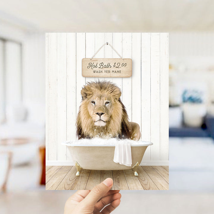 A hand holding a framed image of a lion sitting in a bathtub, with a sign above it that says "Hot Bath $2.00 WASH YER MANE".