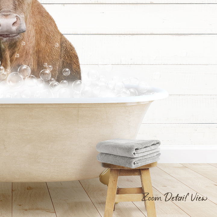 A brown cow is standing in a bathtub filled with bubbles, with a towel and stool nearby.