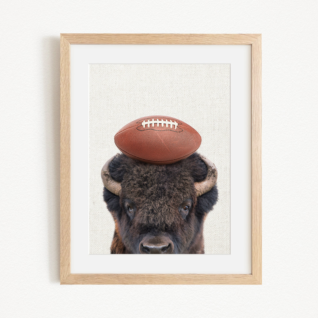 A framed image of a buffalo with a football resting on its head.