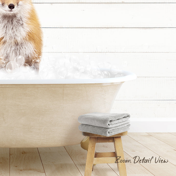 A dog standing in a bathtub filled with bubbles, with a towel and stool nearby.