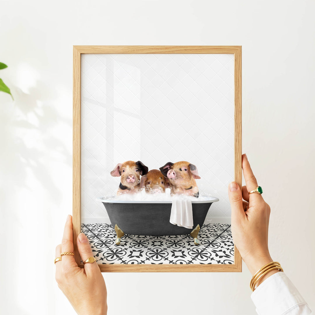 A person's hands are holding a picture frame with a framed image of three adorable baby pigs sitting in a bathtub.