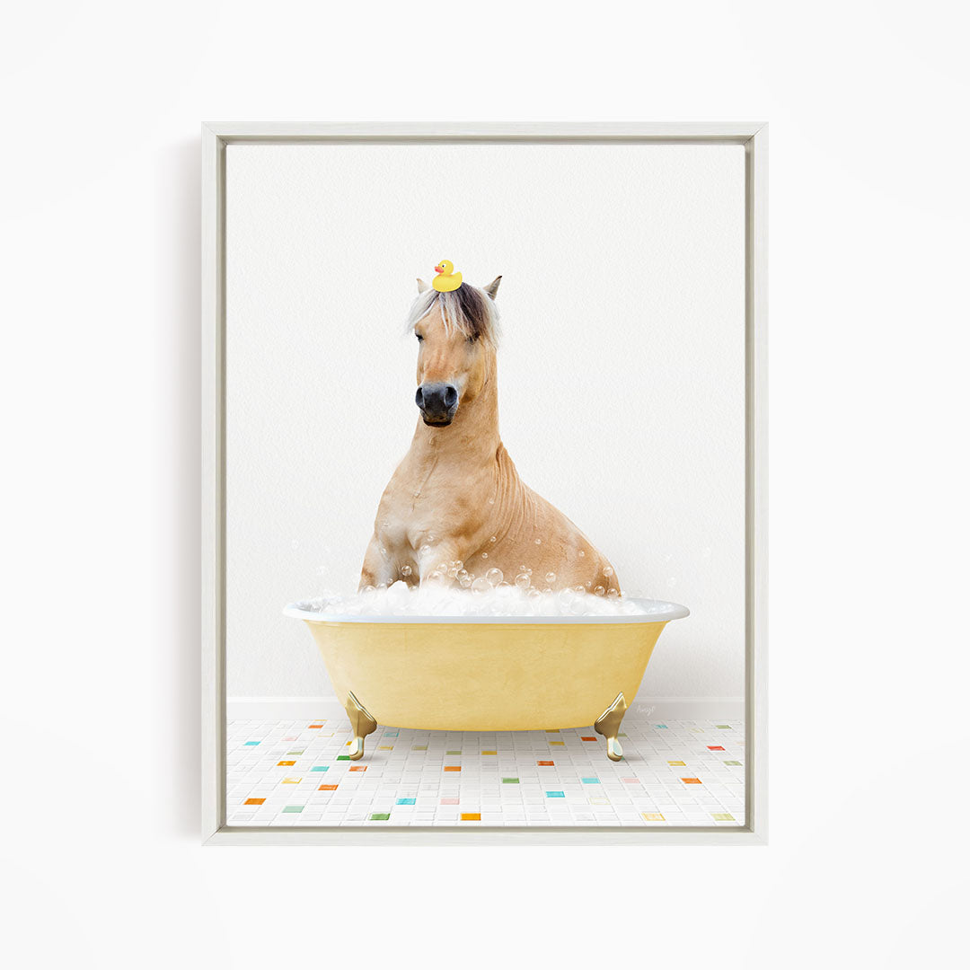 A light brown horse is sitting in a yellow bathtub filled with bubbles, wearing a yellow rubber duck on its head.