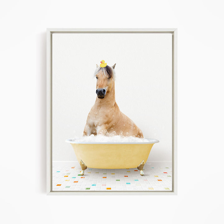 A light brown horse is sitting in a yellow bathtub filled with bubbles, wearing a yellow rubber duck on its head.