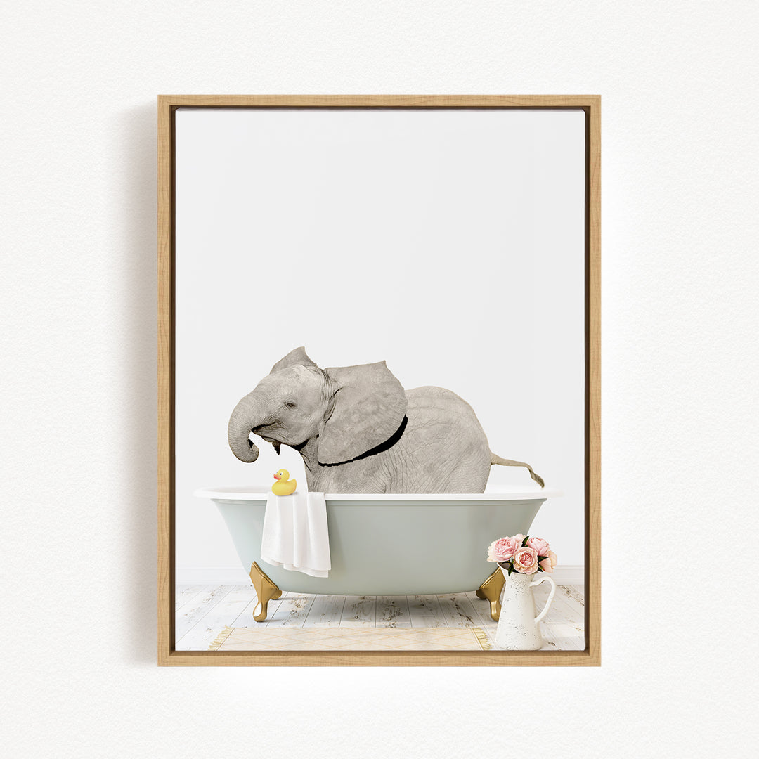 A gray elephant is sitting in a bathtub, holding a yellow rubber duck, with a vase of pink flowers and a white pitcher nearby.