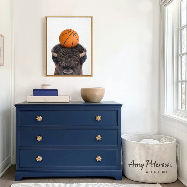 a blue dresser with a framed picture of a buffalo resting on a basketball on top of it. The dresser is situated in a room with white walls and a window.