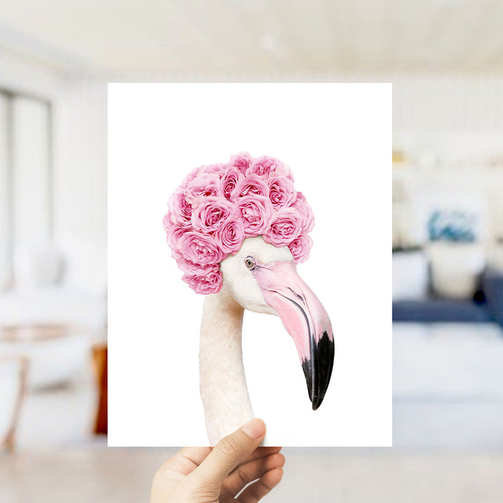 A hand holds up a framed image of a flamingo with a pink flower crown on its head.