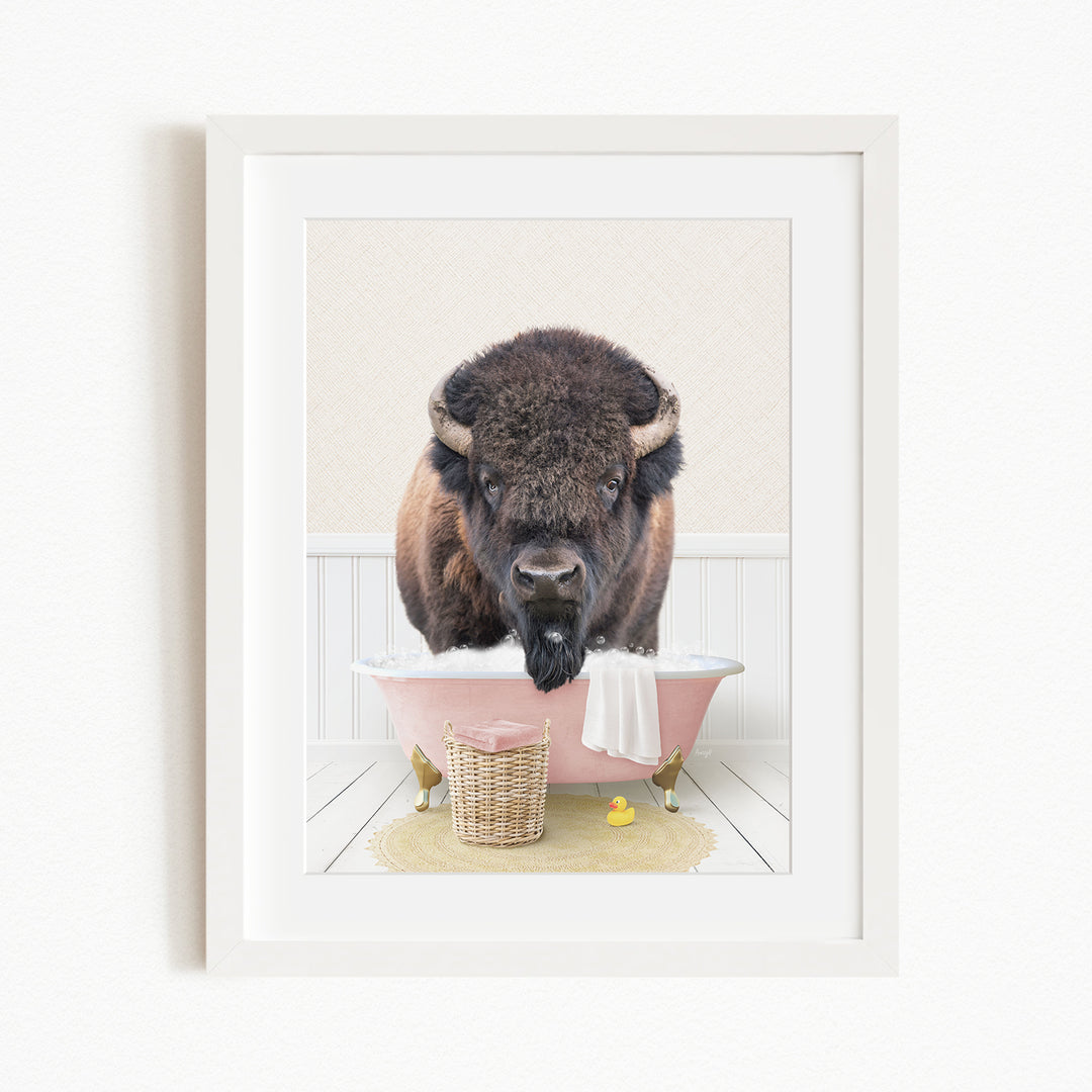 A buffalo standing in a pink bathtub, with a basket of rubber ducks nearby.