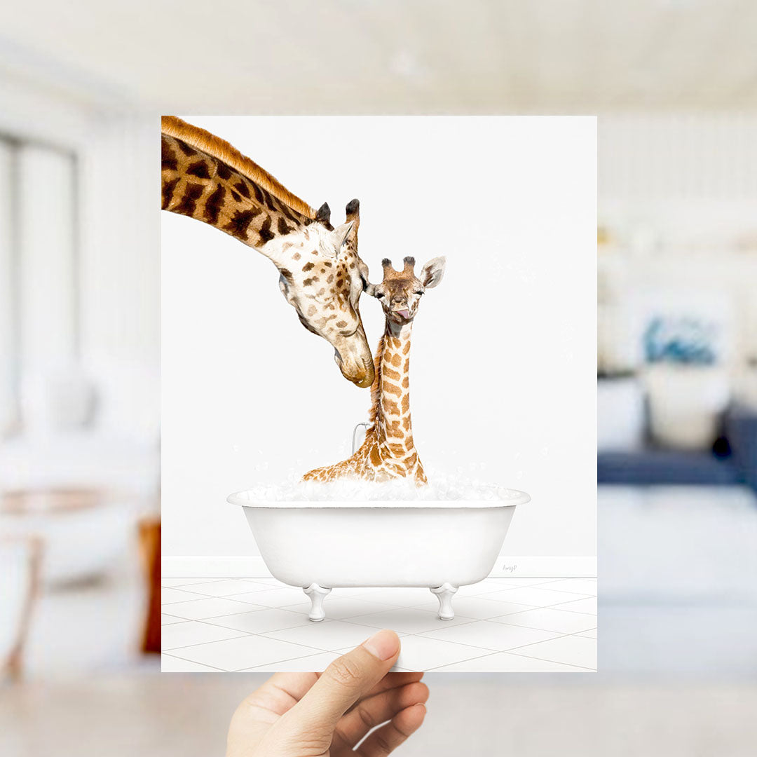A hand holds up a framed image depicting two giraffes in a white bathtub, with one giraffe appearing to be bathing the other.