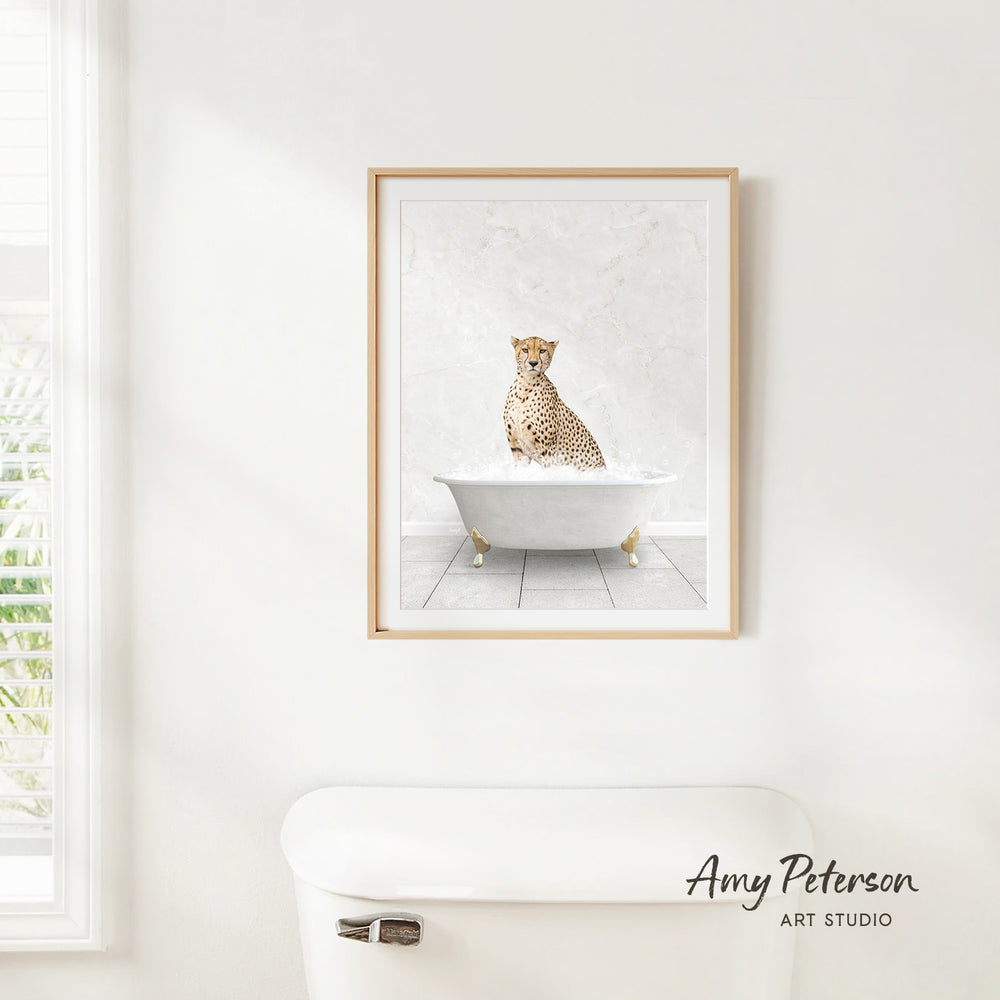 A framed print of a cheetah sitting in a bathtub is hanging on a white wall.