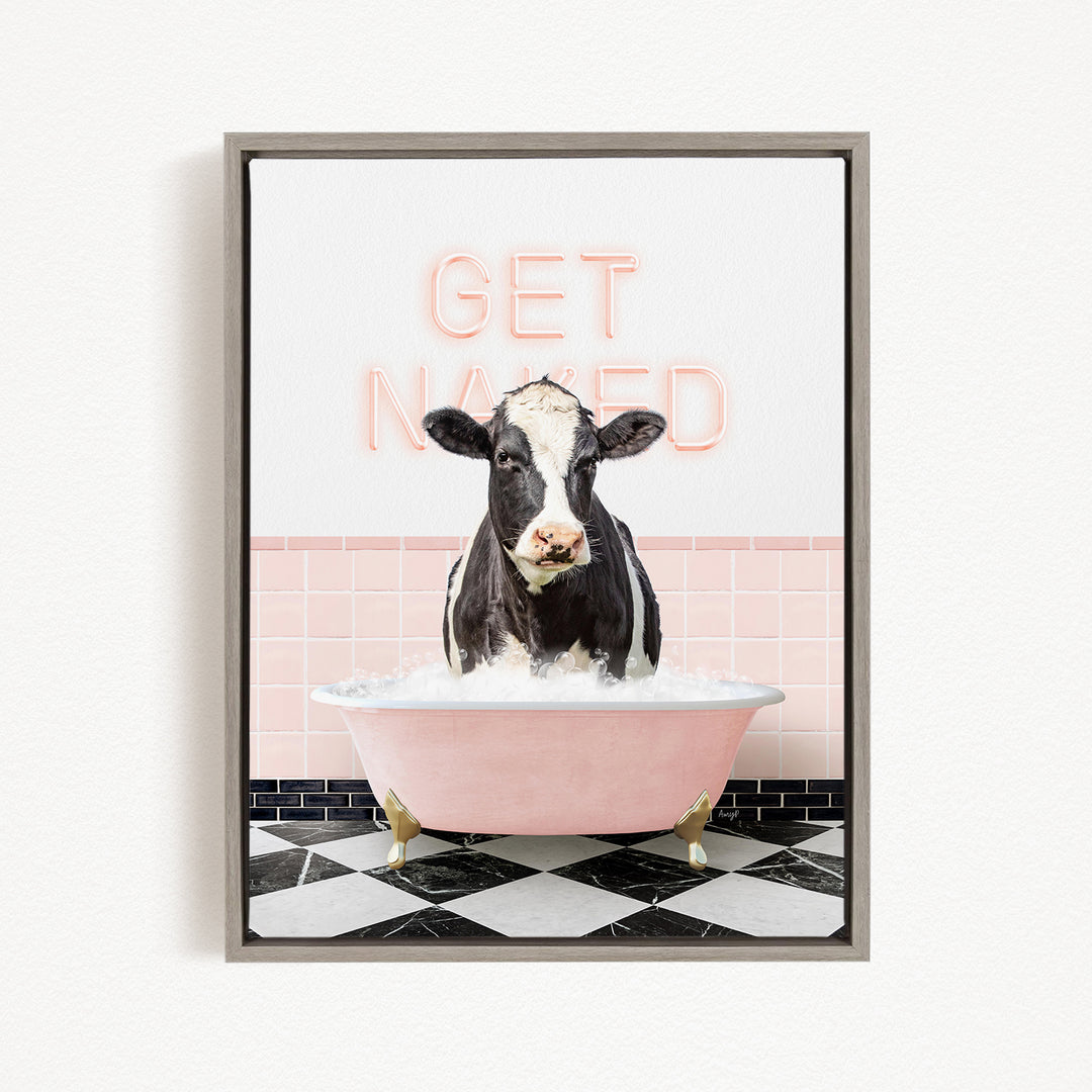 A black and white cow is sitting in a pink bathtub filled with water, with the words "GET NAKED" written in neon pink letters above it.