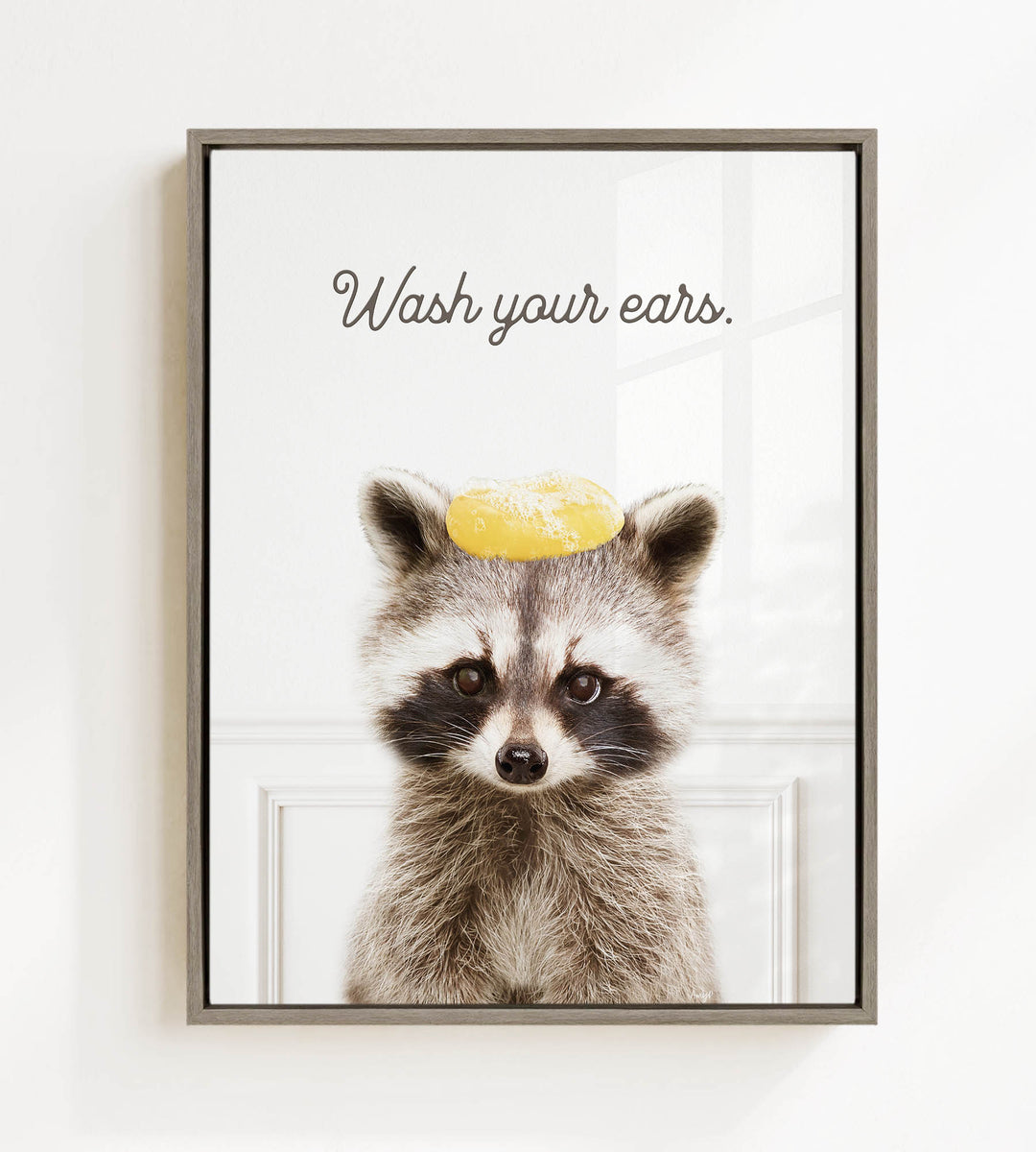 A raccoon wearing a yellow hat with the text "Wash your ears" written on it.