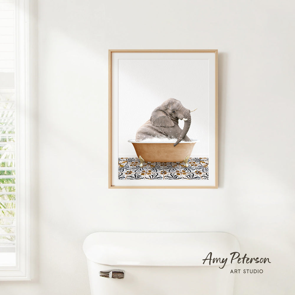 A framed image of a baby elephant sitting in a bathtub, with a patterned tile on the floor.