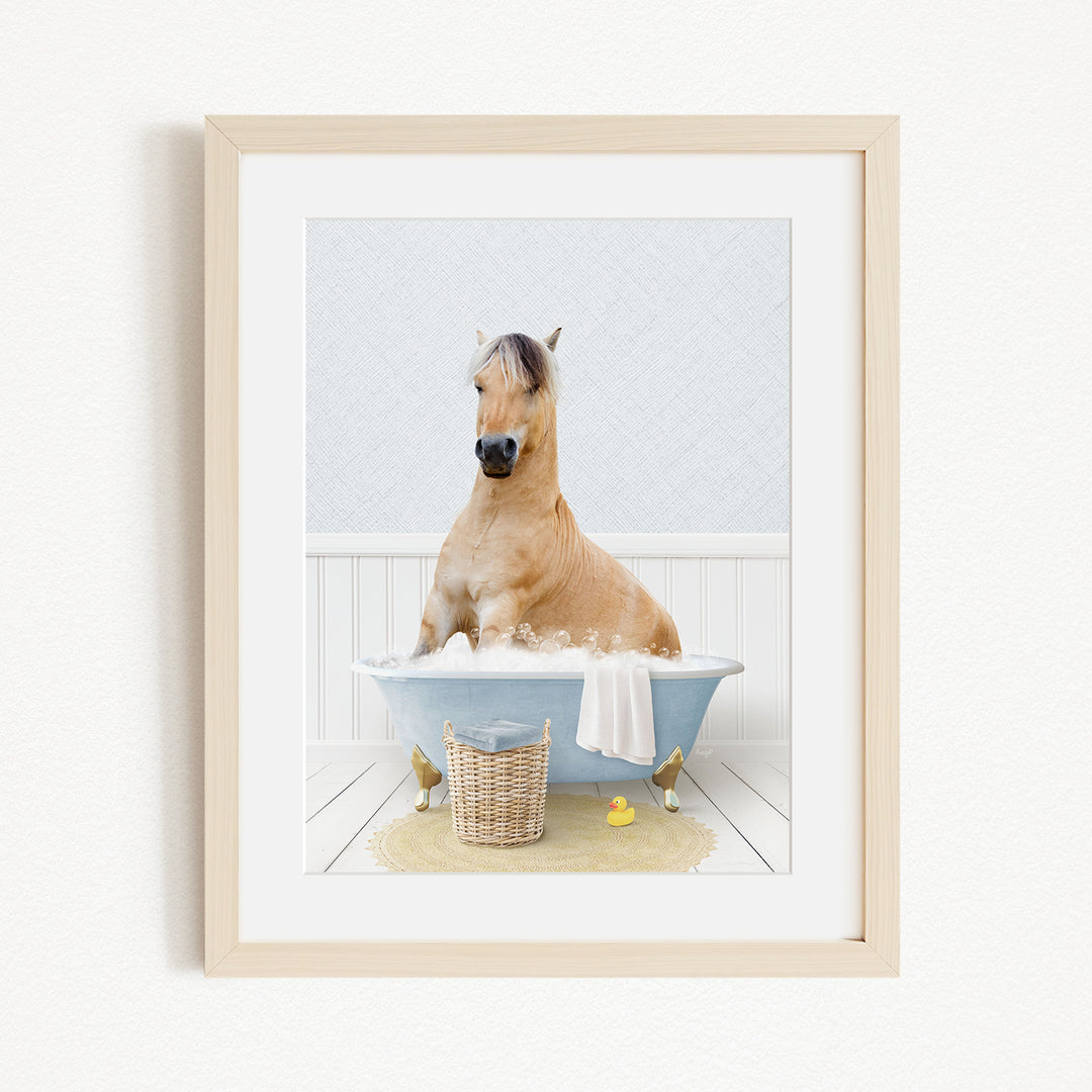 A light brown horse is sitting in a blue bathtub filled with water, surrounded by a yellow rubber duck and a basket.