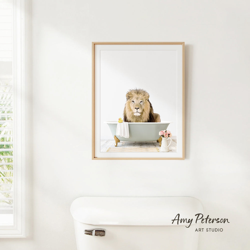 A framed image of a lion sitting in a bathtub, with a vase of flowers and a white toilet in the foreground.