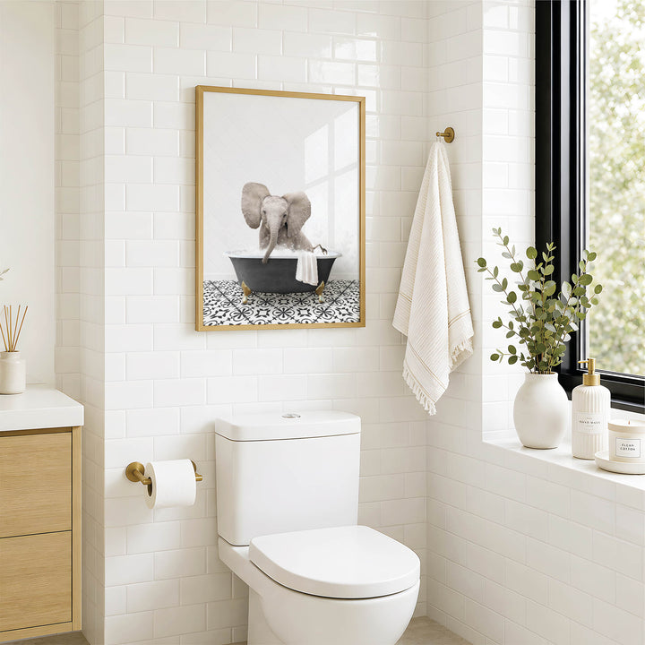 A bathroom with a white toilet, a framed picture of an elephant in a bathtub, and a window with greenery on the sill.