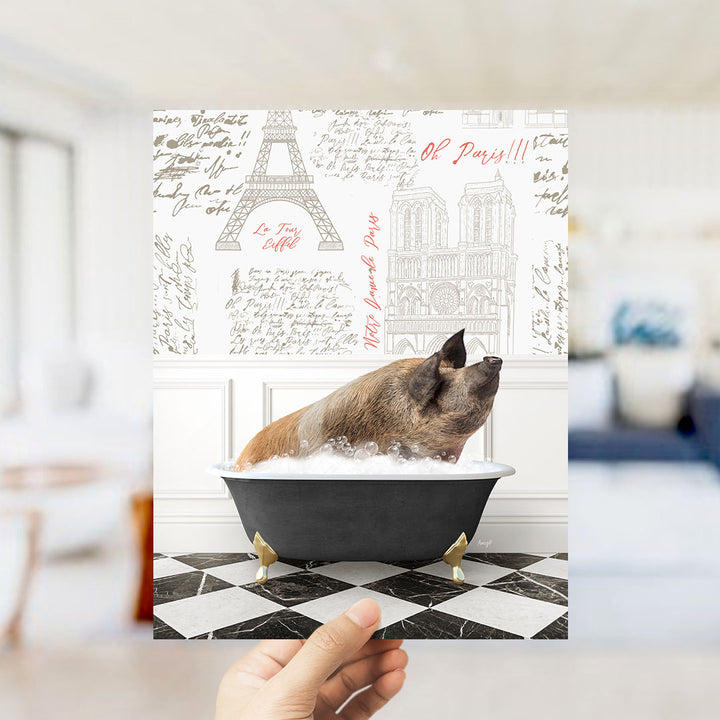 A hand holds up a printed image featuring a pig sitting in a bathtub filled with bubbles, with a Paris-themed background.