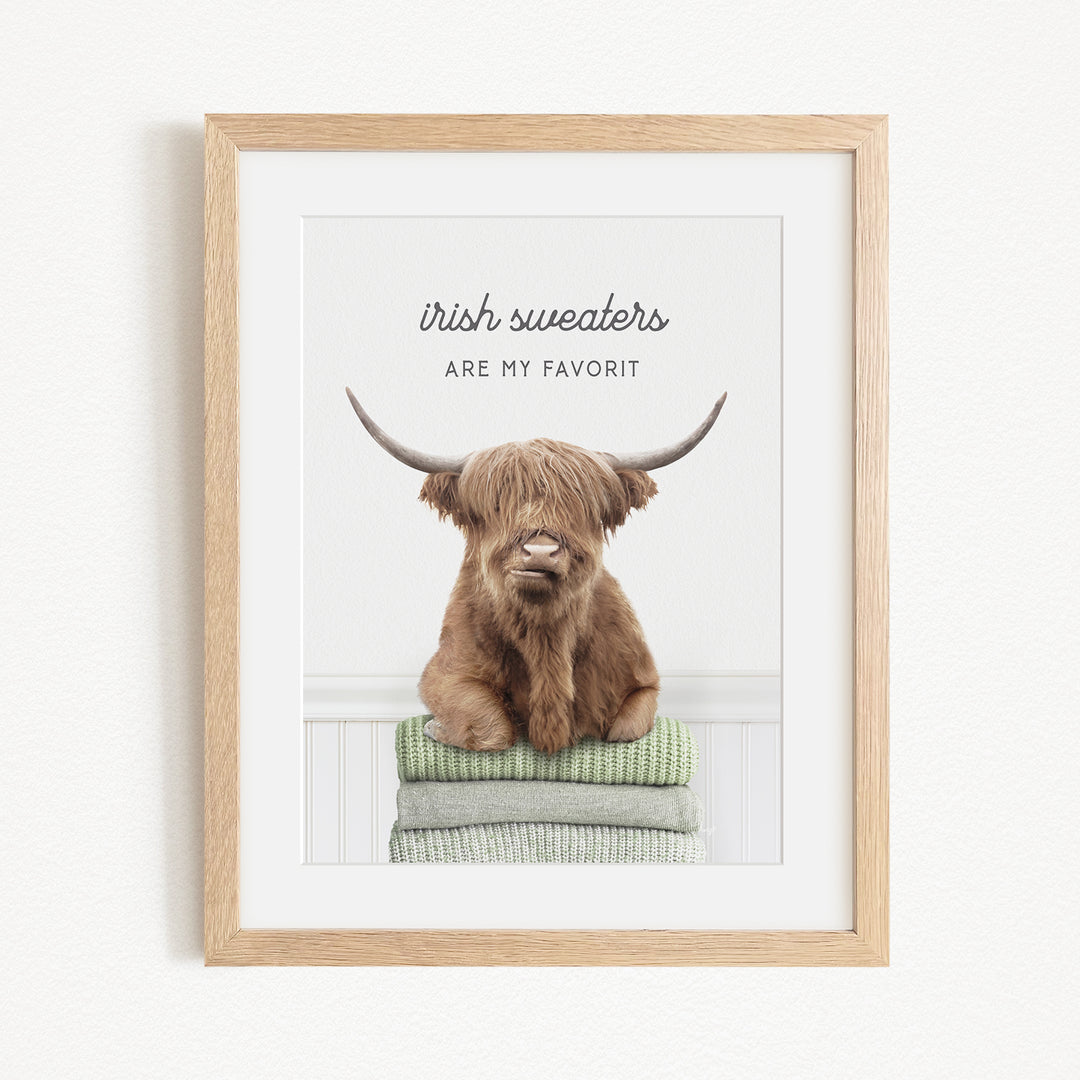 a brown cow with long horns sitting on a stack of green and gray sweaters, with the text "Irish sweaters are my favorite" written above the cow.