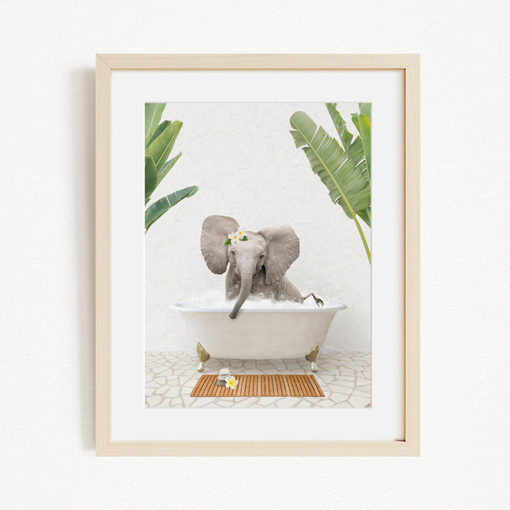 A baby elephant sitting in a bathtub filled with water, surrounded by green leaves and a wooden mat on the floor.