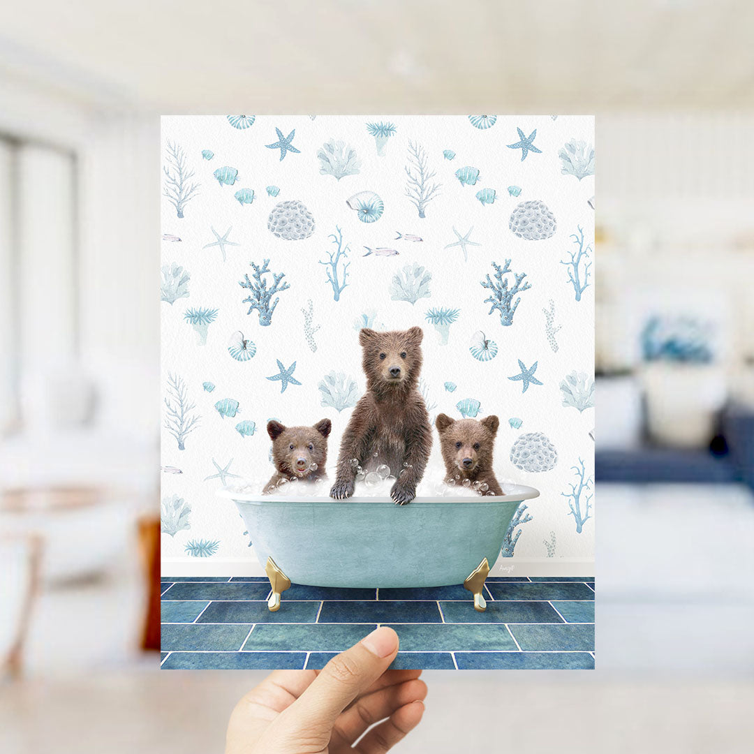 A hand is holding up a print featuring three bears sitting in a bathtub filled with water, surrounded by a pattern of seashells, starfish, and other marine life.