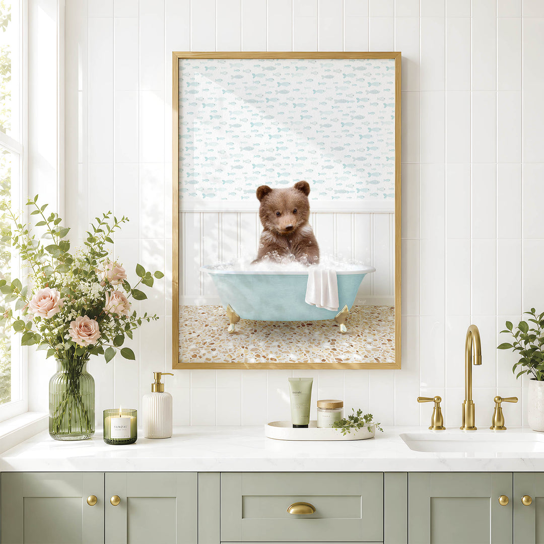 A framed image of a bear sitting in a bathtub, surrounded by flowers and a green vase, is displayed on a white tiled wall above a bathroom sink.