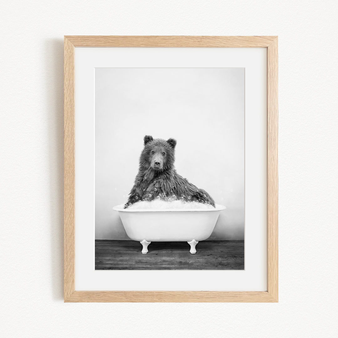 A black and white photograph of a bear sitting in a bathtub filled with water.