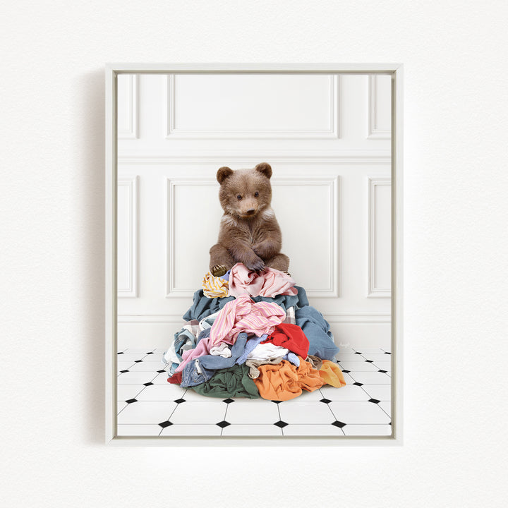 A teddy bear sitting atop a pile of clothes on a tiled floor.