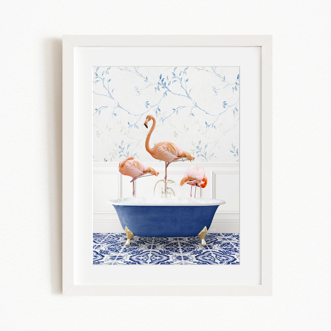 A framed image depicting three pink flamingos standing in a blue bathtub, with a patterned tile floor and a floral wallpaper in the background.