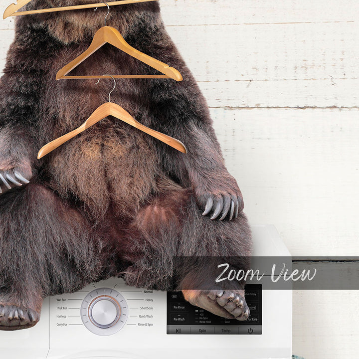 A stuffed bear sitting on a washing machine with clothes hanging from it.