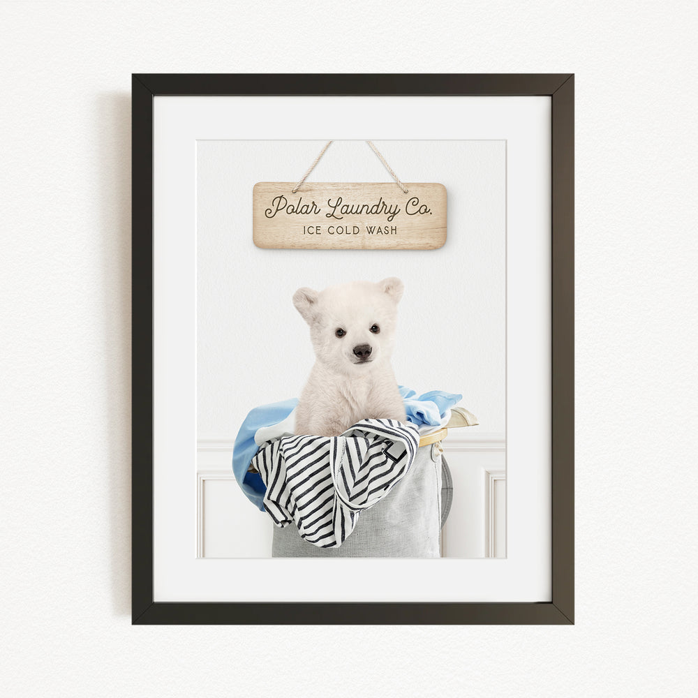 A framed image of a white dog sitting in a laundry basket, with a sign above that reads "Polar Laundry Co. Ice Cold Wash".
