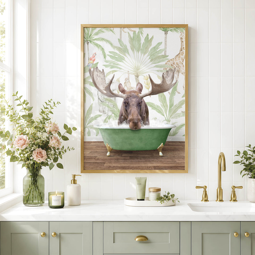 a framed picture of a moose sitting in a bathtub, surrounded by a tropical forest scene. The moose has large antlers and is partially submerged in the green bathtub. The picture is hung on a wall above a white countertop with various bathroom accessories, such as a soap dispenser, a candle, and a vase with flowers.