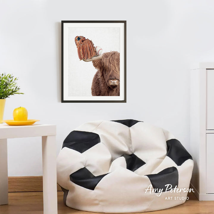 a framed picture of a cow with a baseball glove on its head, hanging on a white wall above a black and white bean bag chair.