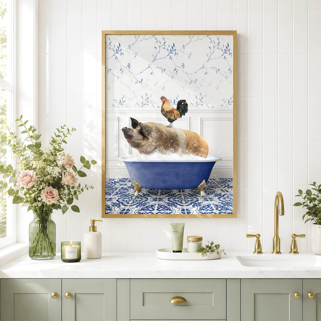 A framed image of a pig sitting in a blue bathtub, with a rooster perched on its back, is displayed on a white tiled wall above a bathroom counter with various toiletries and a vase of flowers.