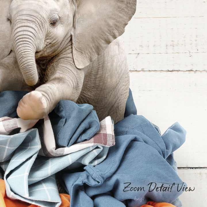 A baby elephant resting on a pile of clothes, with its trunk curled up.