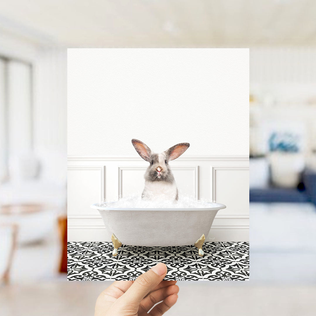 A white rabbit sitting in a white bathtub filled with water, with a hand holding the photo up to the camera.