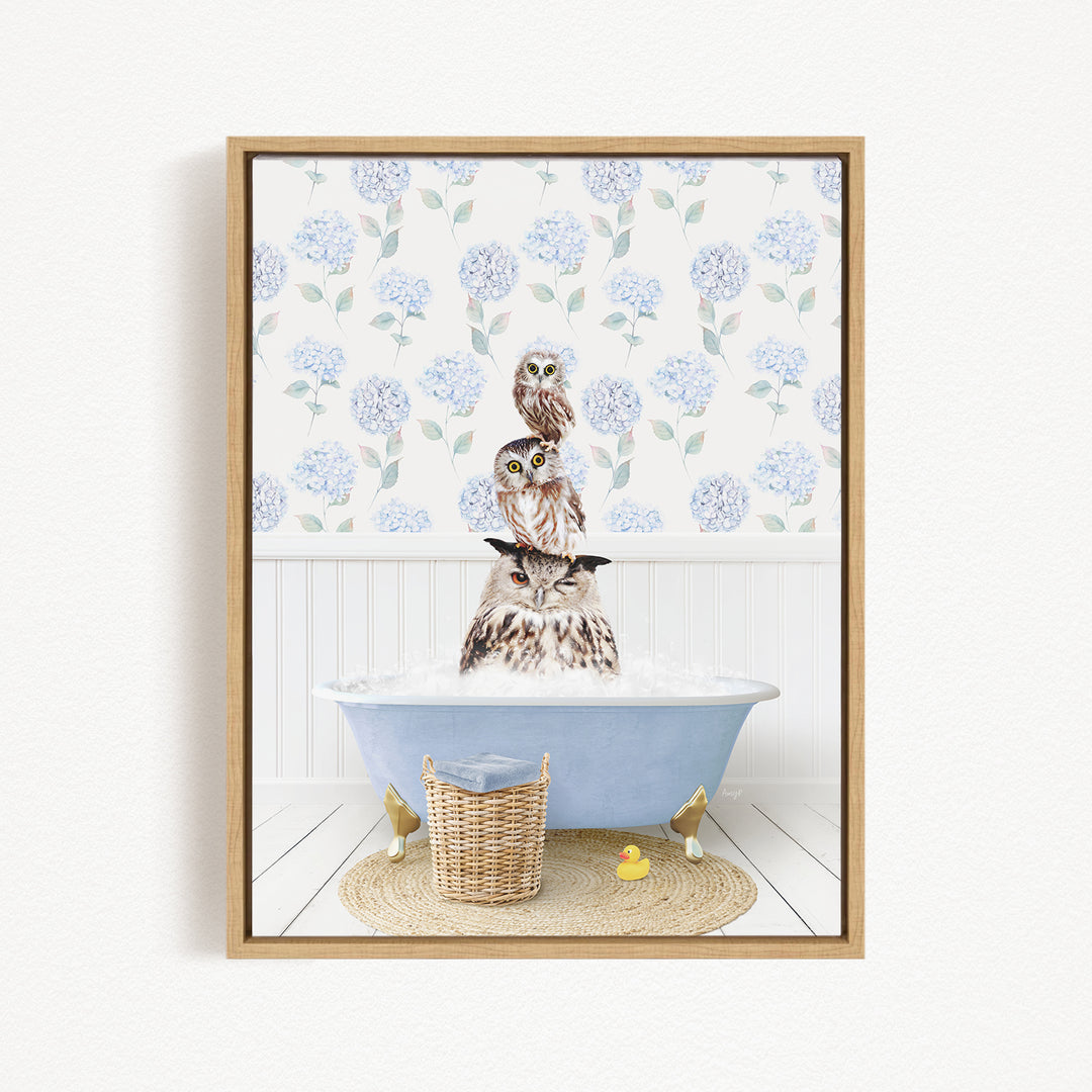 A framed image depicting three owls sitting in a bathtub filled with water, surrounded by a floral patterned wallpaper.