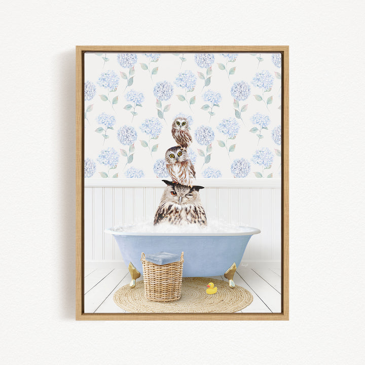 A framed image depicting three owls sitting in a bathtub filled with water, surrounded by a floral patterned wallpaper.
