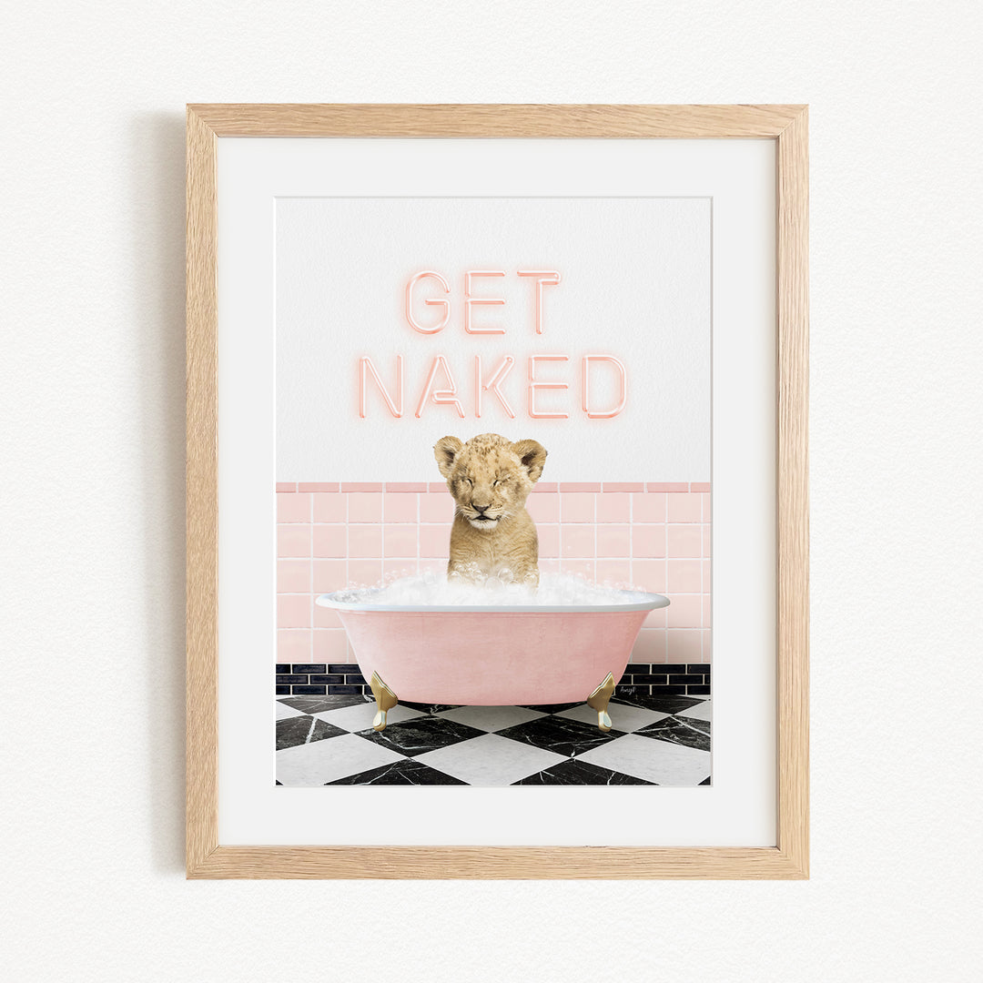 A framed image depicting a young lion cub sitting in a pink bathtub filled with water, with the text "GET NAKED" displayed above it.