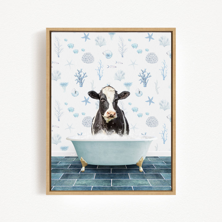 A black and white cow is sitting in a white bathtub filled with water, surrounded by a blue and white floral pattern on the wall behind it.