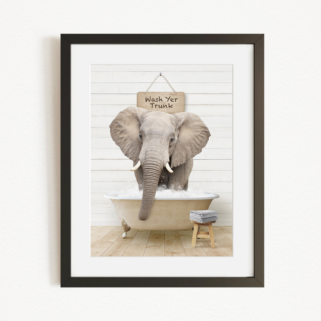 A framed image of an elephant standing in a bathtub, with a sign above it that says "Wash Yer Trunk".