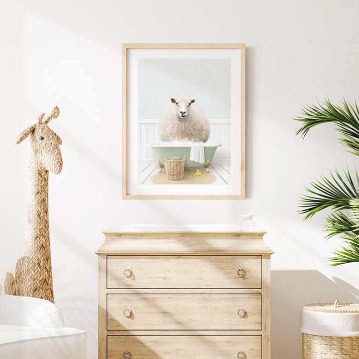 a framed picture of a sheep sitting in a bathtub, surrounded by a basket and a towel, in a cozy and well-decorated room with a wooden dresser and a stuffed giraffe.
