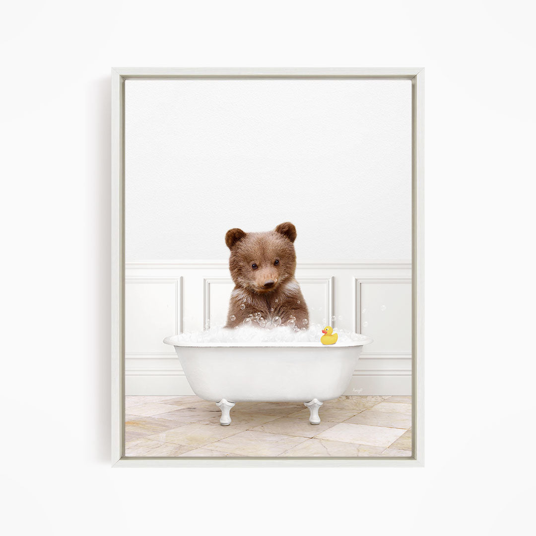 A brown bear sitting in a white bathtub filled with bubbles, with a rubber duck floating nearby.