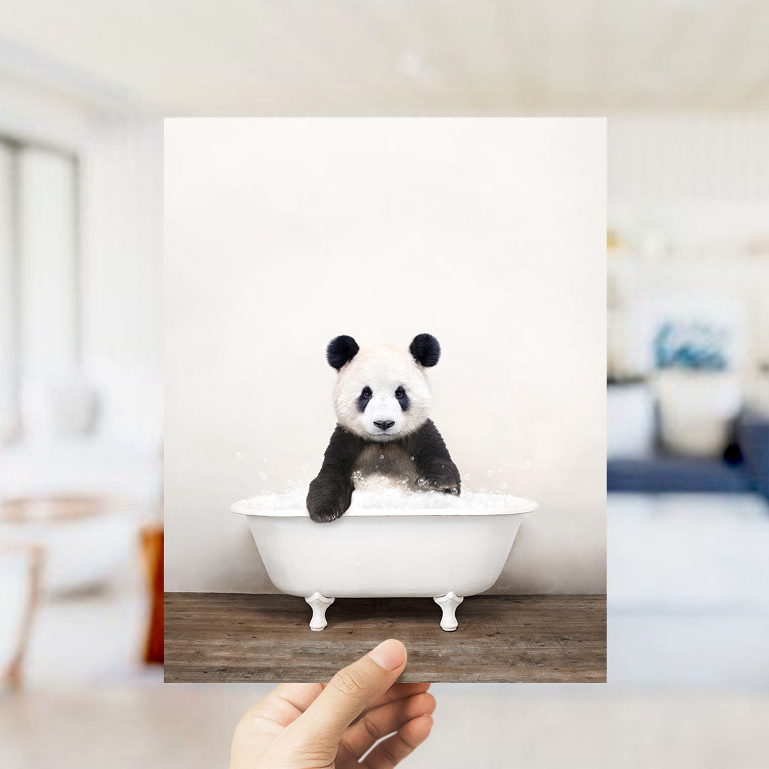 A panda bear sitting in a white bathtub filled with bubbles, with a blurred background suggesting a bathroom setting.