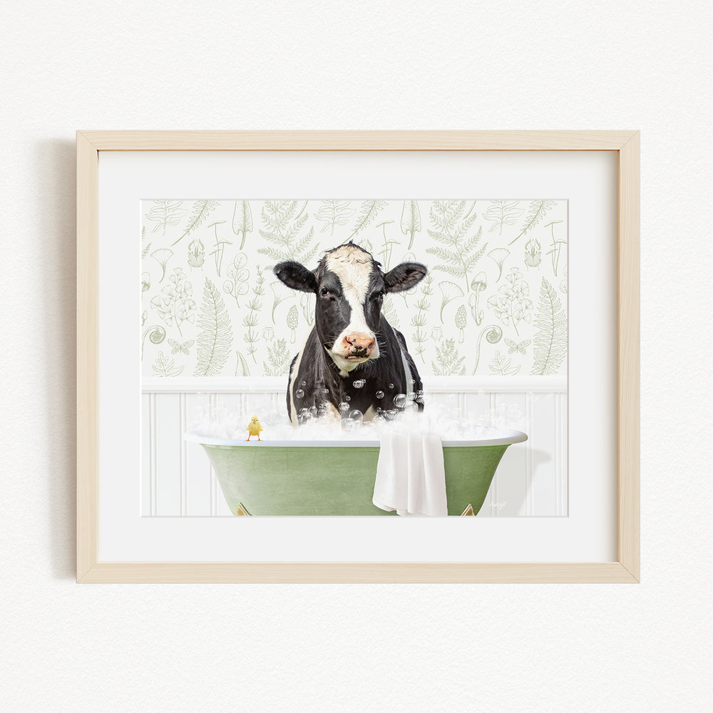 A black and white cow is sitting in a green bathtub filled with bubbles, with a towel draped over the side of the tub.
