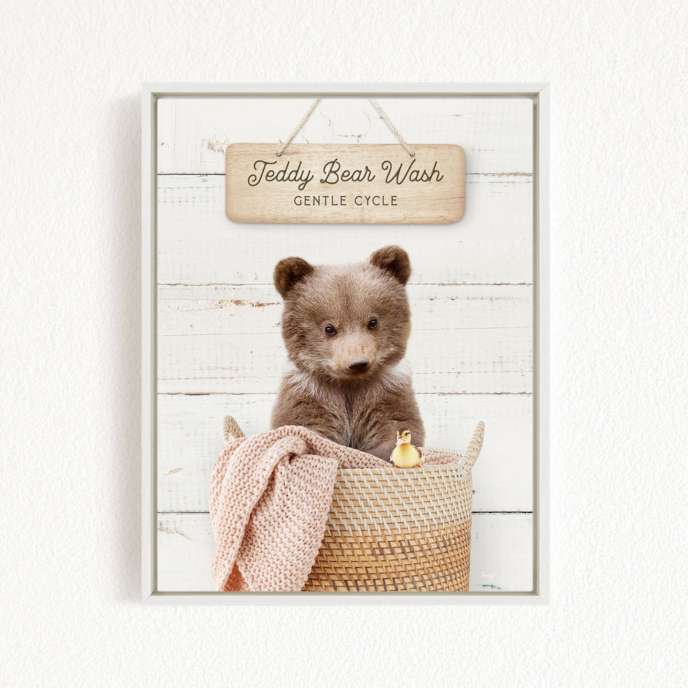 A teddy bear sitting in a woven basket, with a sign above that reads "Teddy Bear Wash Gentle Cycle".