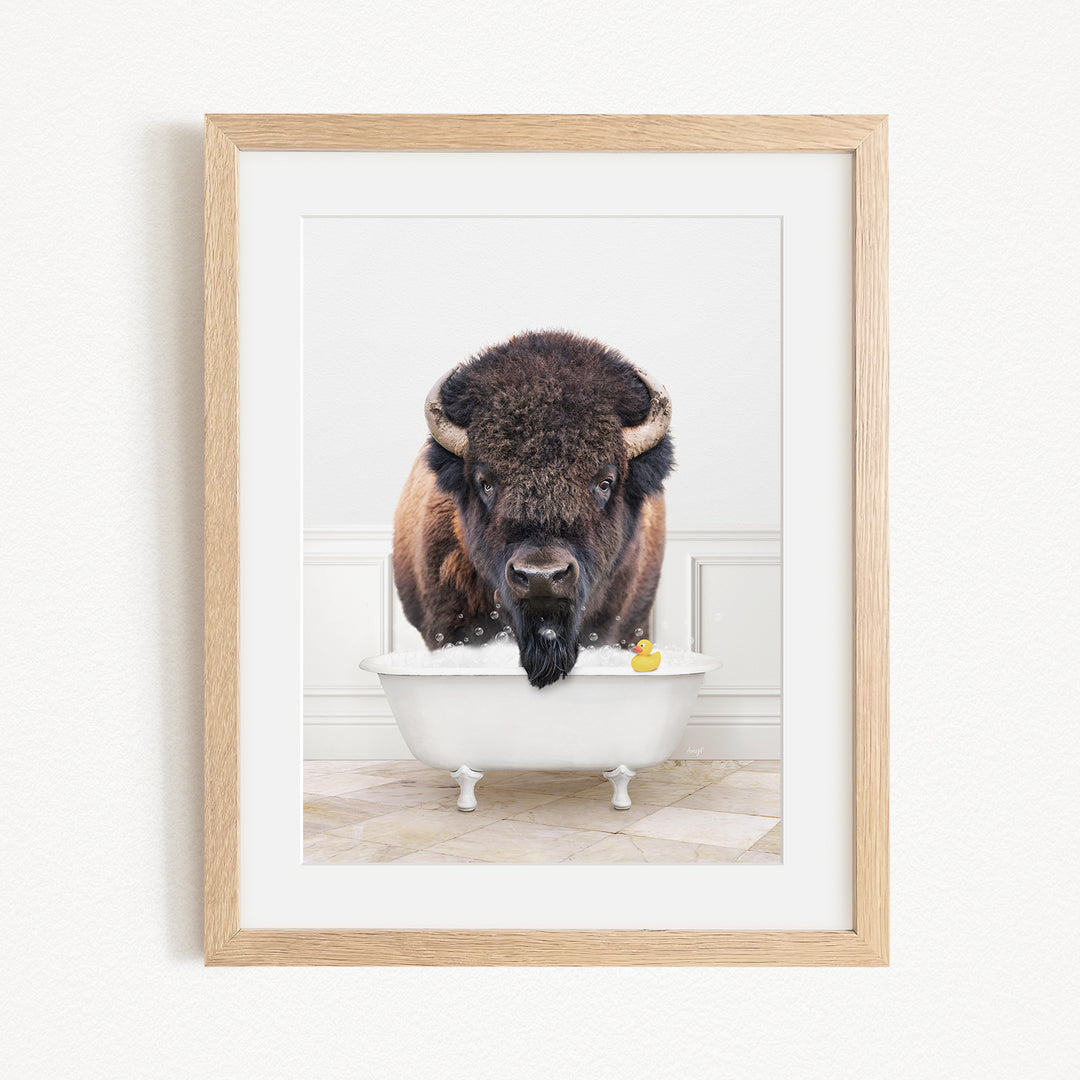 A buffalo with large horns is standing in a white bathtub, with a yellow rubber duck floating in the water.