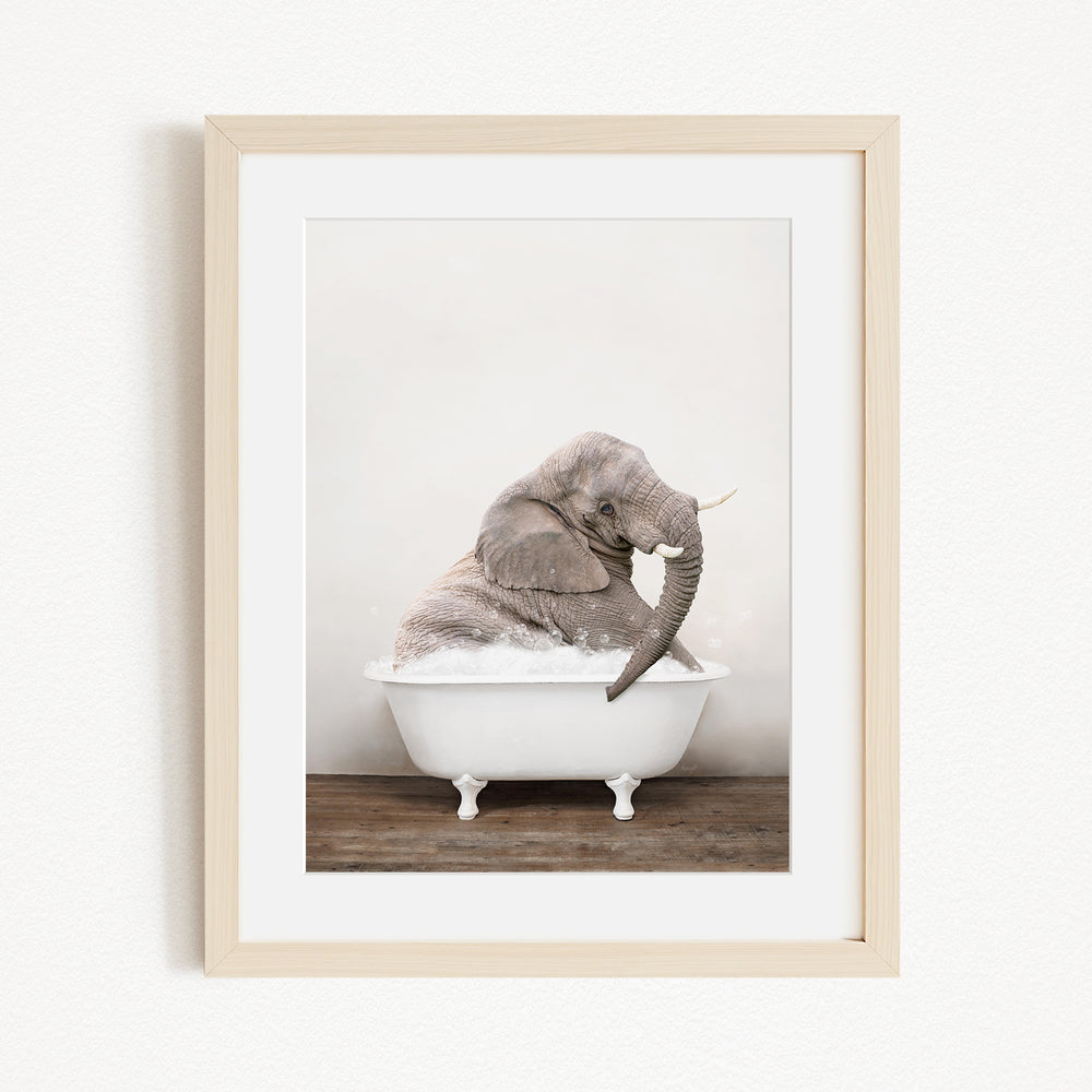 A gray elephant is sitting in a white bathtub, with its trunk raised and appearing to be enjoying the bath.