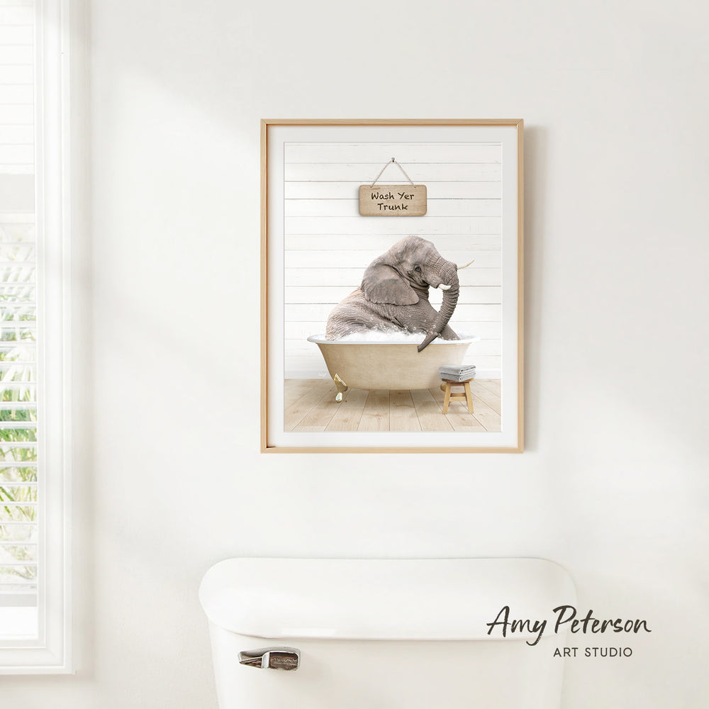 A framed print of an elephant sitting in a bathtub, with a sign above it that says "Wash Your Trunk".