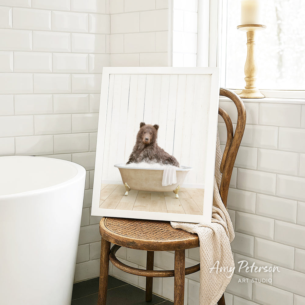 A framed image of a bear sitting in a bathtub, with a towel draped over the side of the tub.