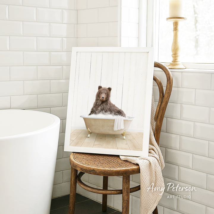 A framed image of a bear sitting in a bathtub, with a towel draped over the side of the tub.
